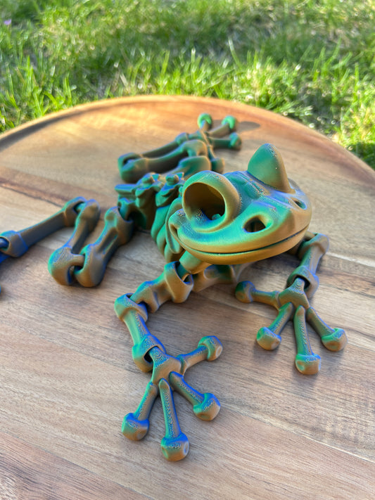 Multicolored 3D Printed Skeleton Frog resting on a circular wooden surface.