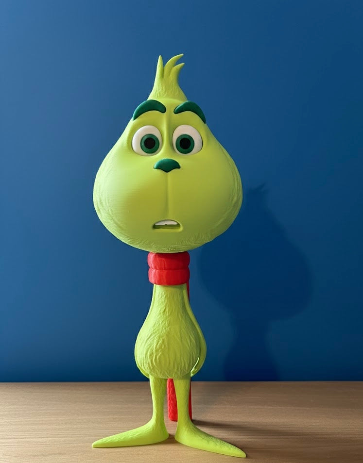 Green Grinch character with a red scarf, standing on a light brown table, against a blue background.