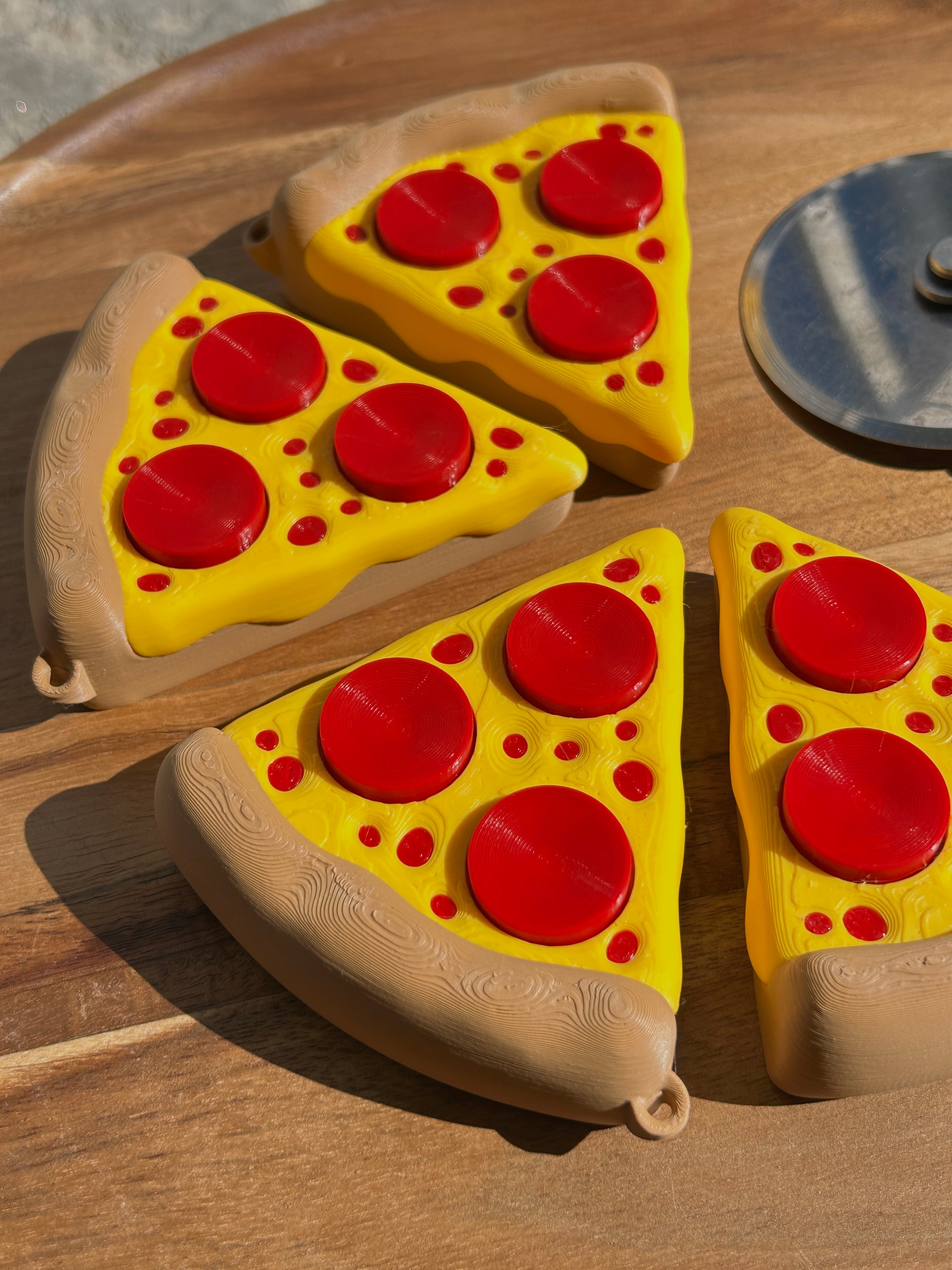 Four Pizza Slice Fidget Clicker Toys on a circular, wooden surface. Pizza cutter blade is partially visible.