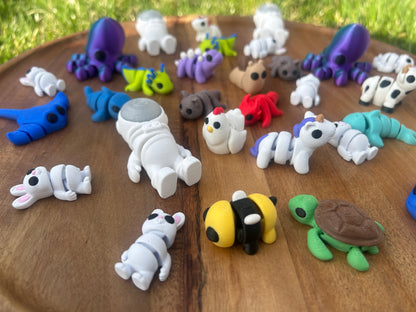 A collection of 3D Printed Mini Critters lays scattered across a circular, wooden platform.