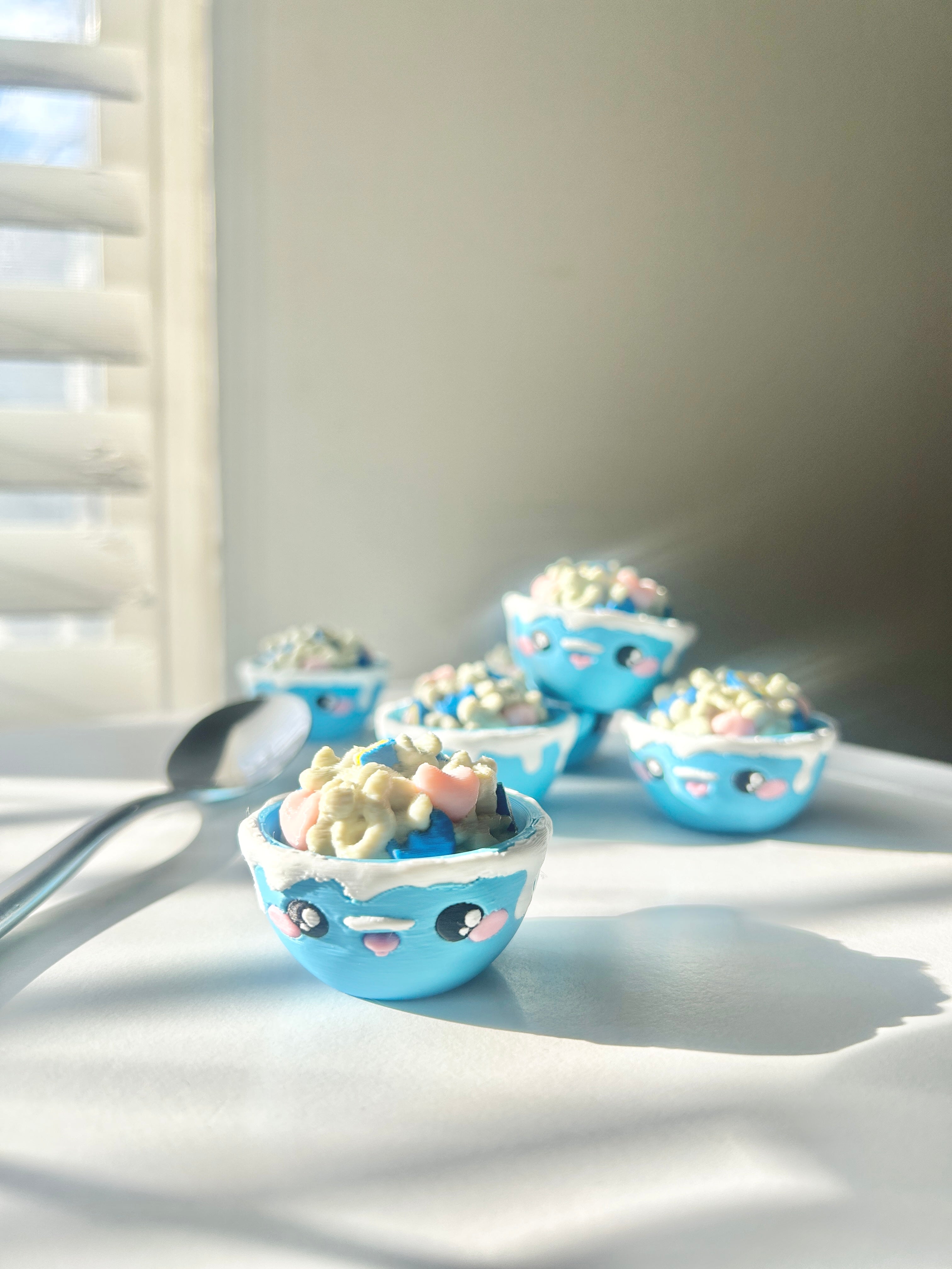 Set of small blue bowls with cartoon faces next to a metal spoon on a white surface.