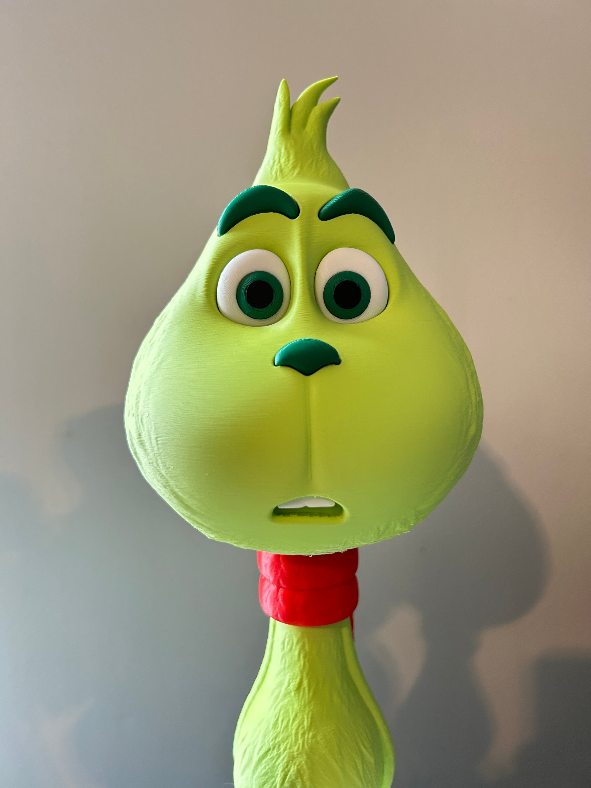 Green Grinch model Christmas decoration with a face and red scarf on a light beige background.