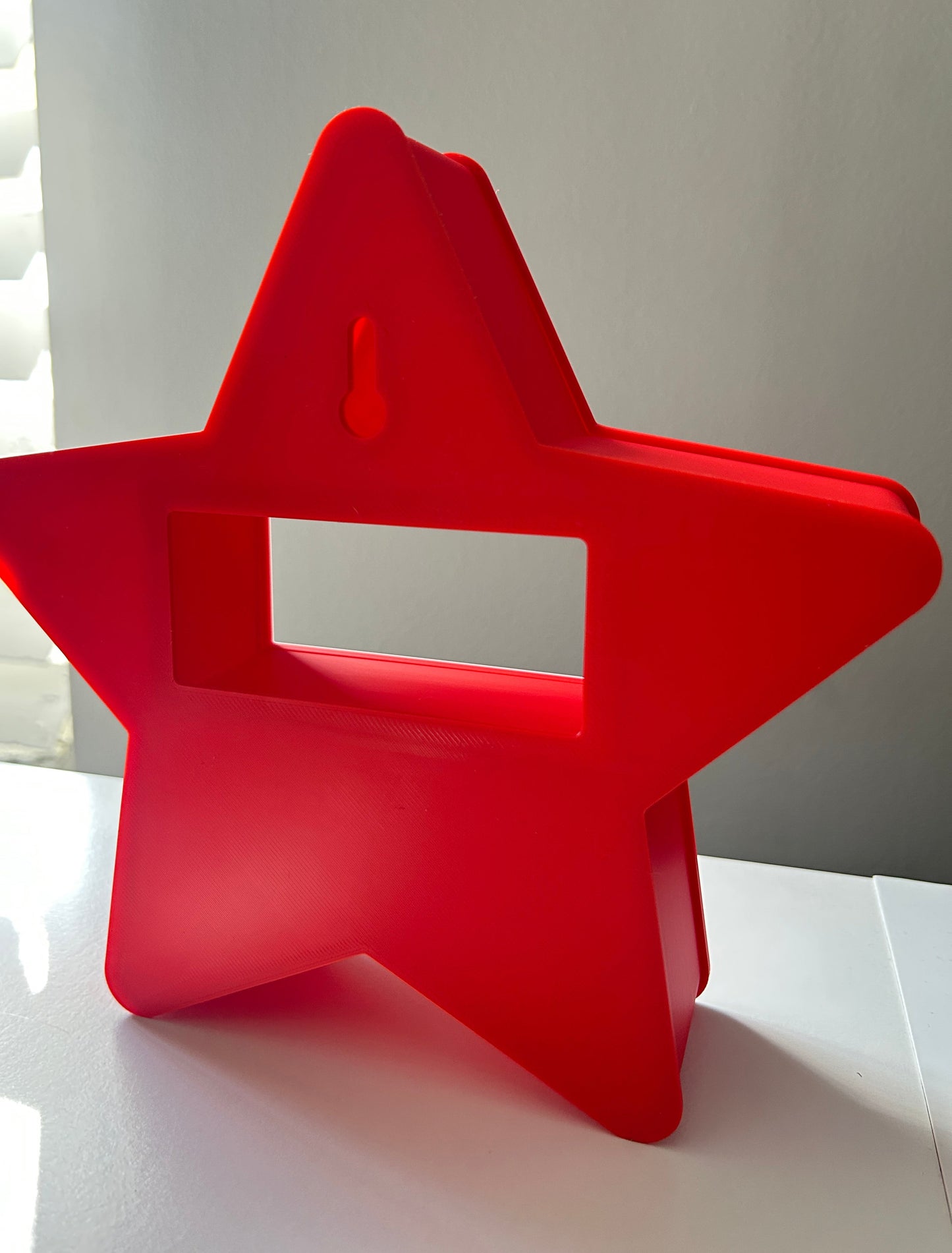 Back view of a red, star-shaped Christmas countdown on a white shelf against a beige-colored surface.