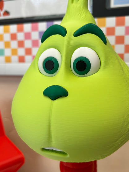 Close-up of a green Grinch model decoration with googly eyes on a blurred background