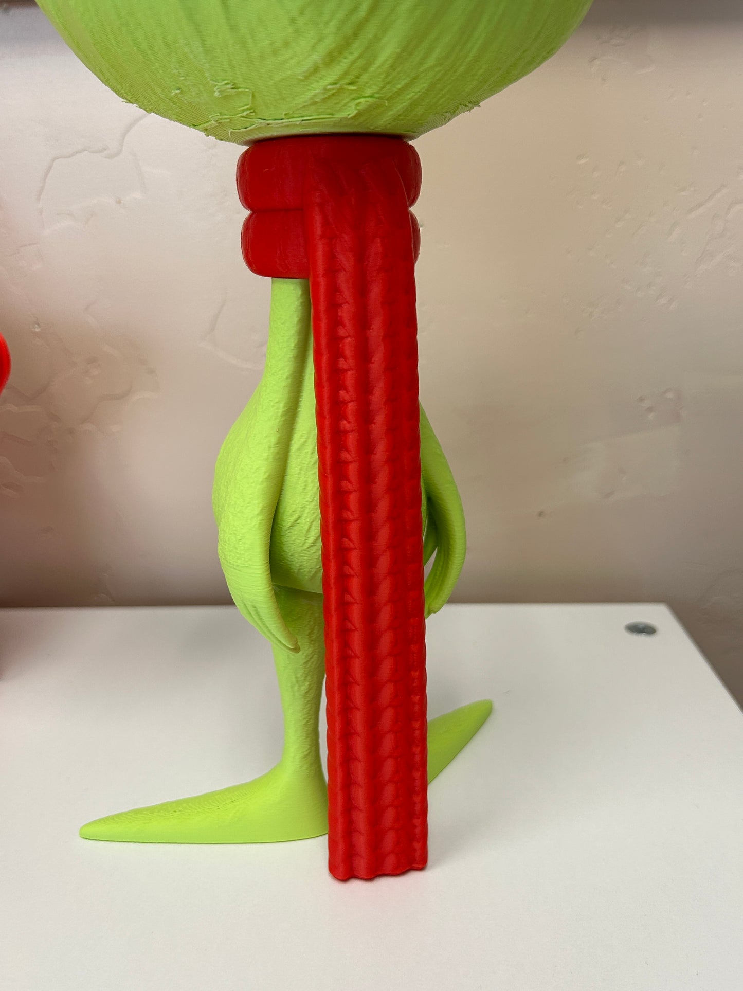 Back view of the red scarf on the green Grinch standing home decor model on a white background
