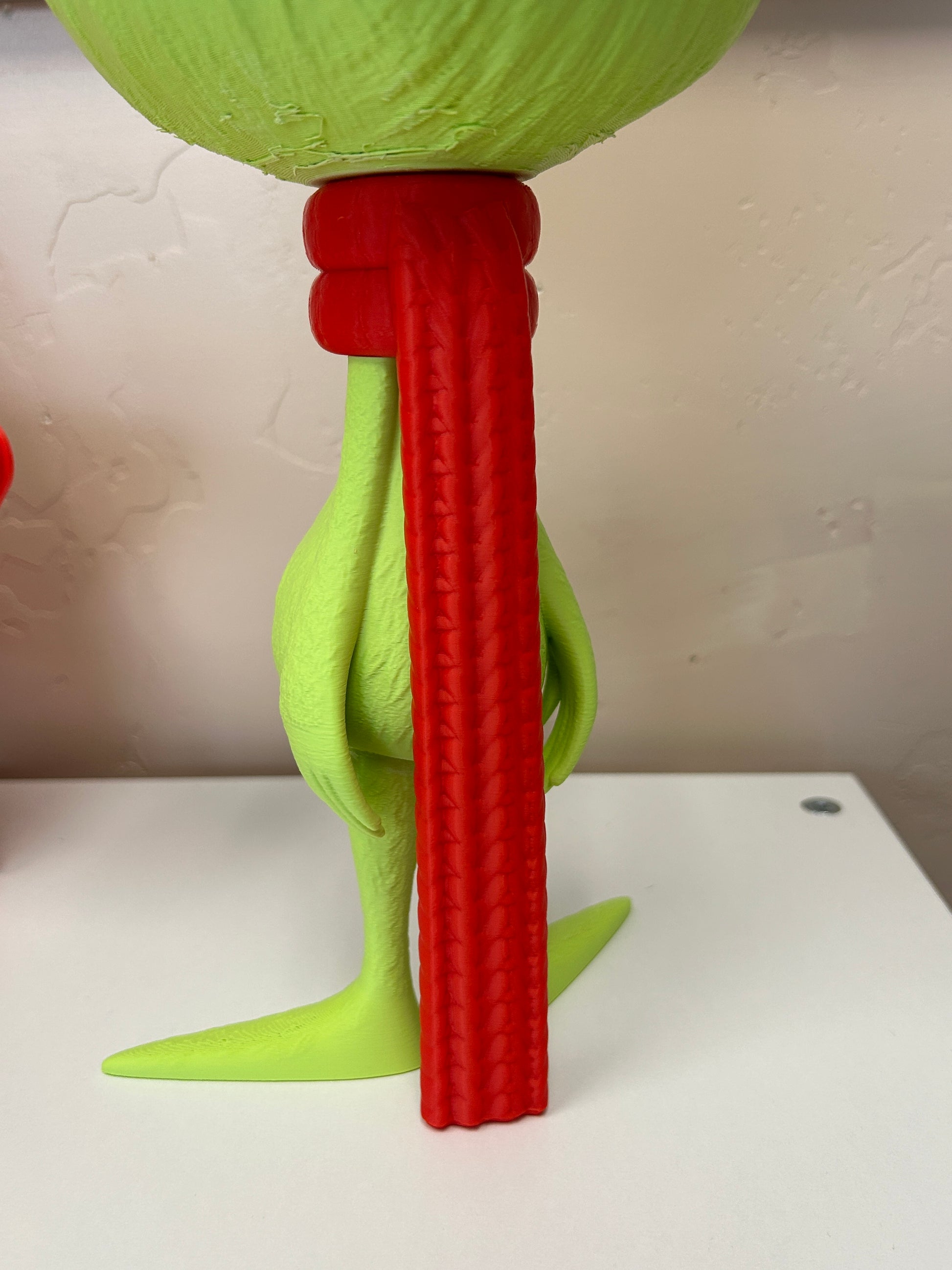 Back view of the red scarf on the green Grinch standing home decor model on a white background