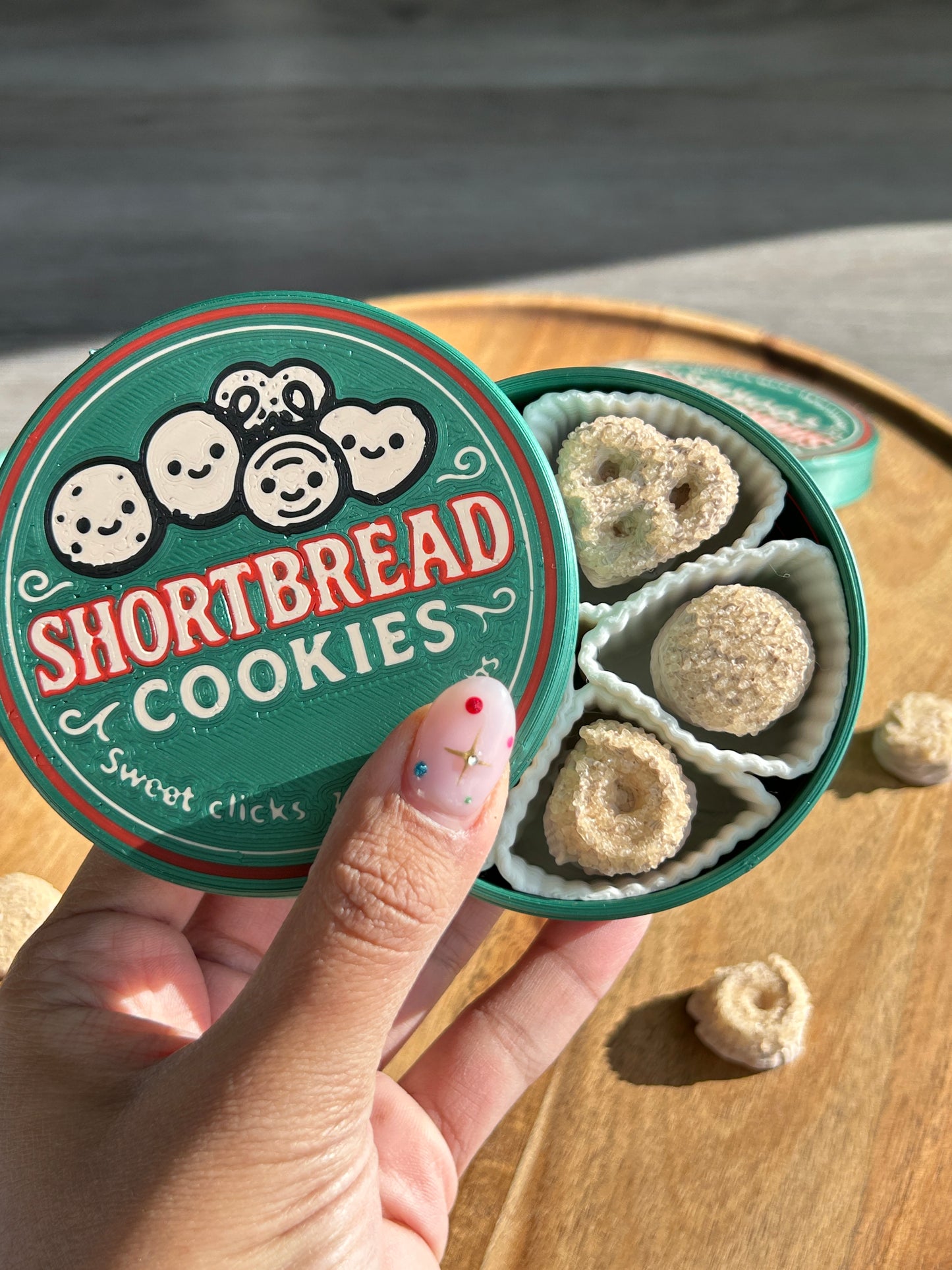 Hand holding a container of shortbread cookies with a decorative lid on a wooden surface.