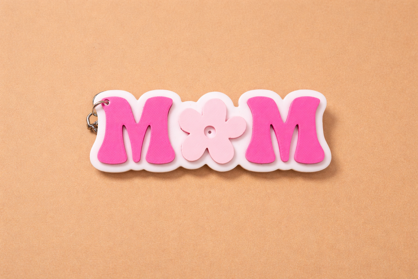 Pink and white 'MOM' keychain on a beige background.