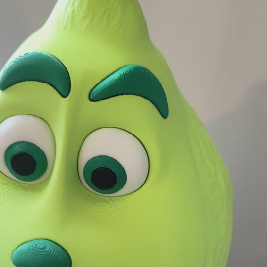 Video pans around a Green Grinch character with a red scarf, standing on a white table, against a beige-colored background.