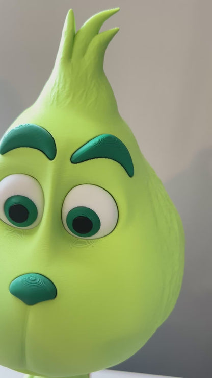 Video pans around a Green Grinch character with a red scarf, standing on a white table, against a beige-colored background.