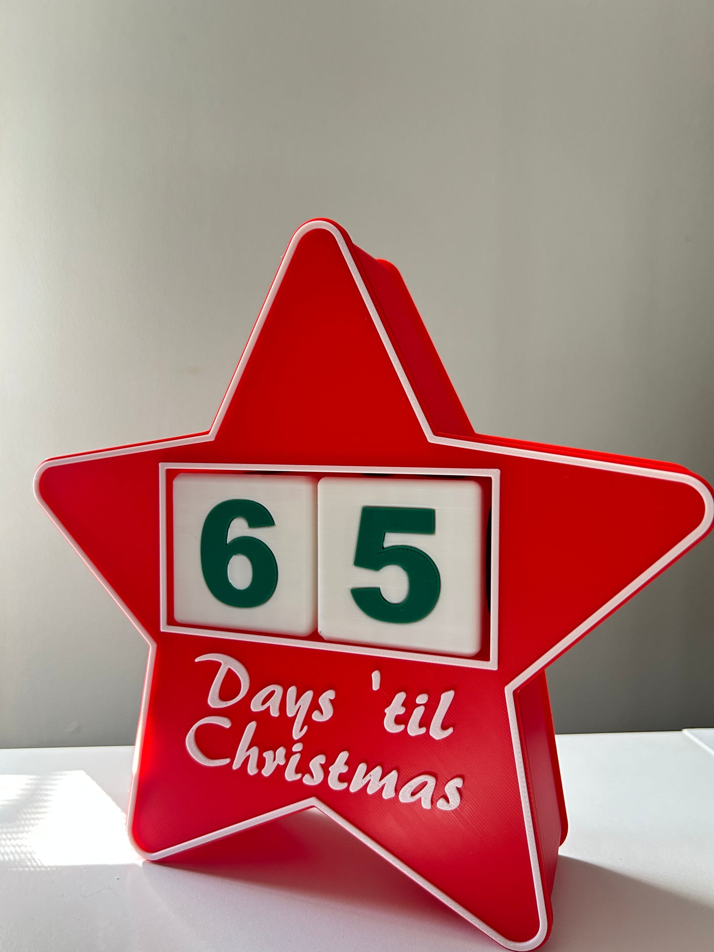 Red star-shaped Christmas countdown sign with numbers '6' and '5' on a white shelf.