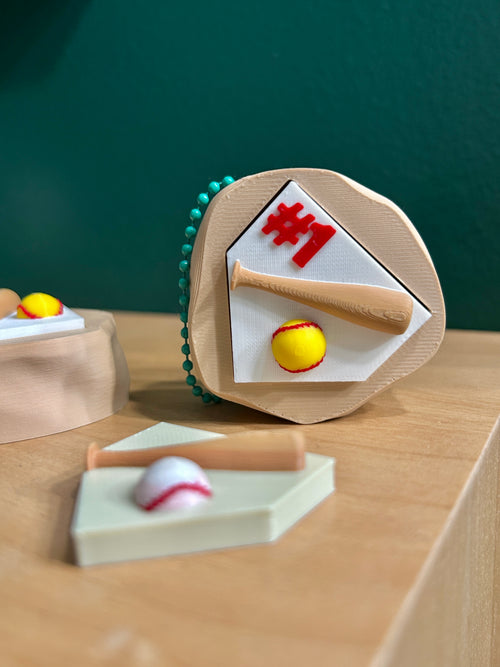 3D printed mound of dirt with home plate and softball laying next to bat next to #1 text. Baseball clicker topper below.
